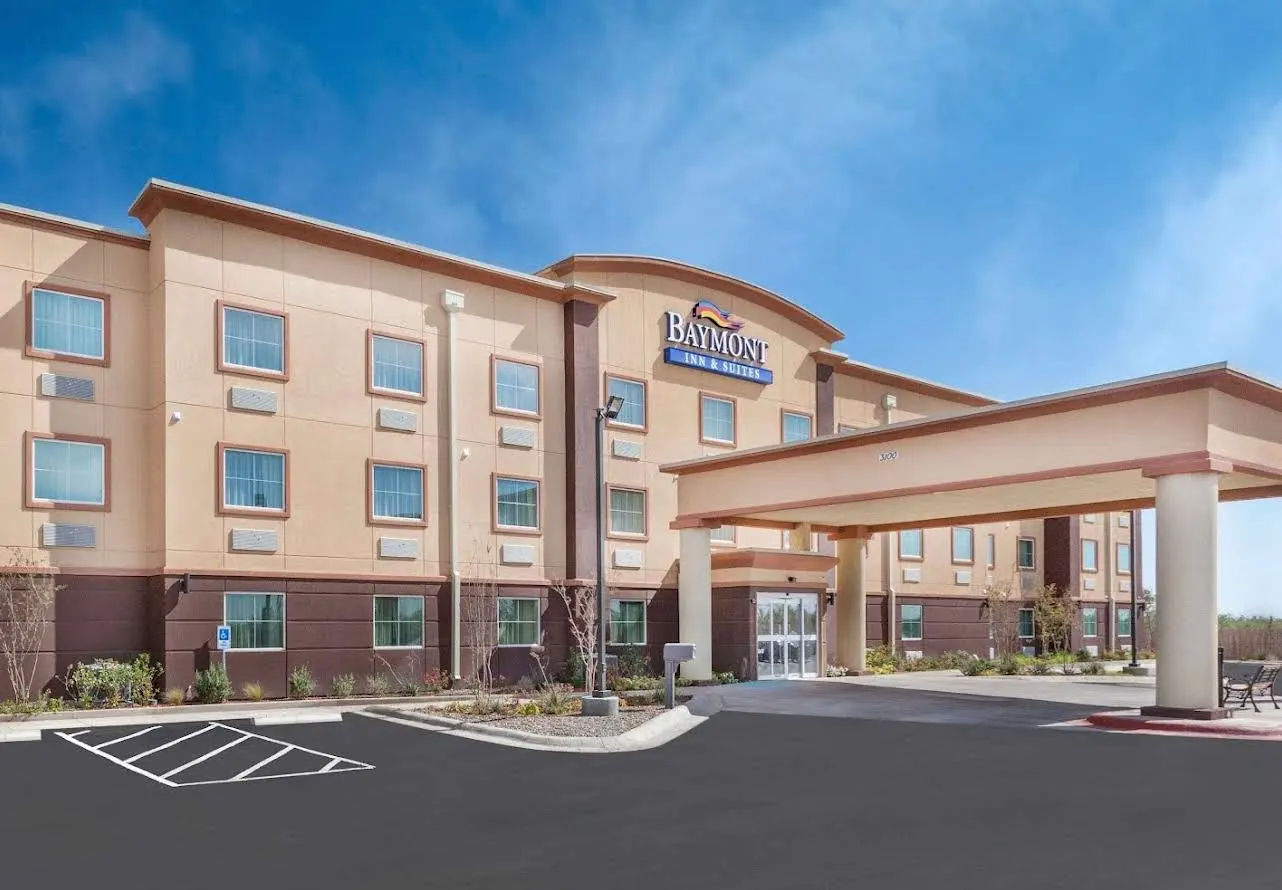 A Baymont Inn & Suites in tan stucco, its porte-cochère at the right under a clear sky