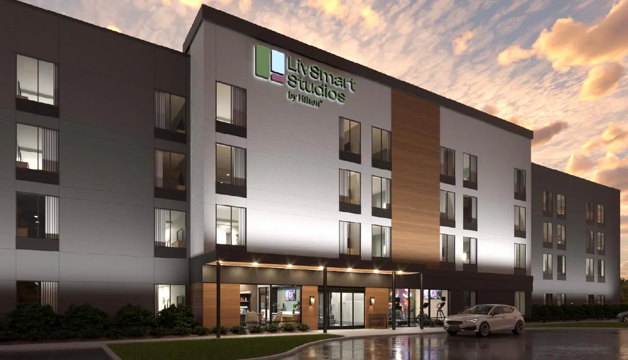 Rendering of a LivSmart Studios by Hilton at sunset, a wood-clad bay over the lit entrance canopy