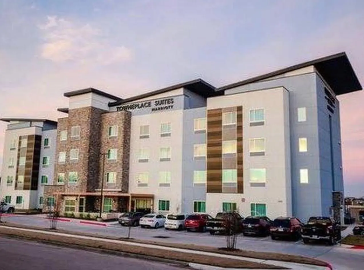 A four-storey TownePlace Suites by Marriott at dusk, stone tower at the entrance, cars parked in front