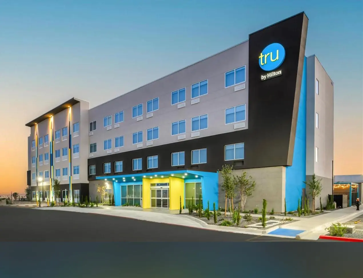 A Tru by Hilton at sunset, its blue and yellow entrance lit beneath the round blue sign